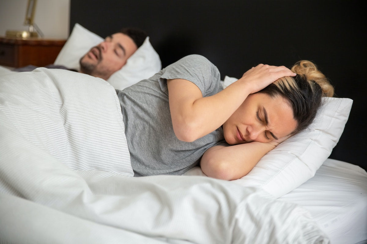 woman covering her ears unable to sleep next to her snoring partner